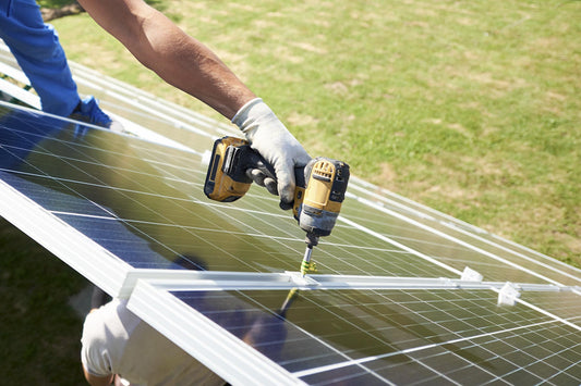 A solar installer uses an electric screwdriver to install ground-mounted solar panels in a yard