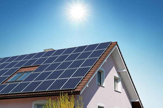 A large home's roof covered in solar panels with the sun shining above it