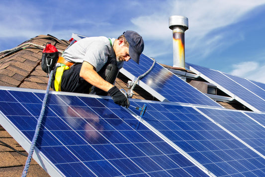 A homeowner wearing a blue baseball cap and a safety harness installs rooftop solar panels