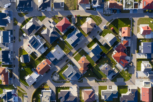An aerial view of a suburban neighborhood with colorful houses, many of which have rooftop solar panels