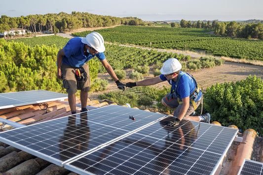 Two contractors collaborate to complete a solar panel installation on a tile roof next to a ranch