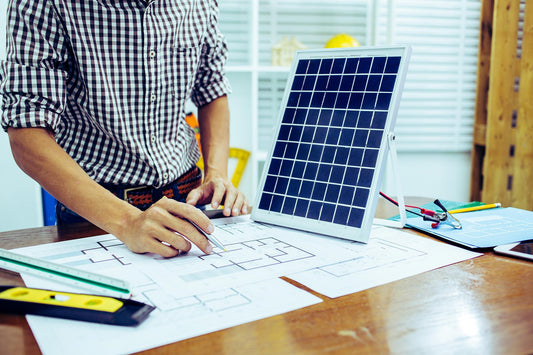 A person in a checkered button-down stands at a table while drawing on a diagram next to a solar panel model